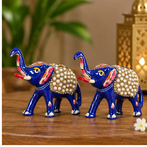 Pair of blue elephant showpieces for shelf and console decoration
Hand-painted metal figurines with glossy blue finish
Red and white accents decorate the standing elephant figures
Pearl-style bead embellishments form decorative saddles
Compact elephant pair for desks, mantels and entryways
Handcrafted Indian-inspired home décor accents
Uphar Handicrafts