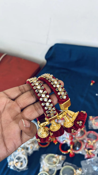 Maroon silk thread bangles with Kundan stonework
Gold-tone embellishments decorate the bangle surface
Jhumka latkan provides a hanging ornamental detail
Metal base covered with silk thread wrapping
Set of two traditional Indian bangles
Festive jewelry for traditional dressing
Uphar Handicrafts