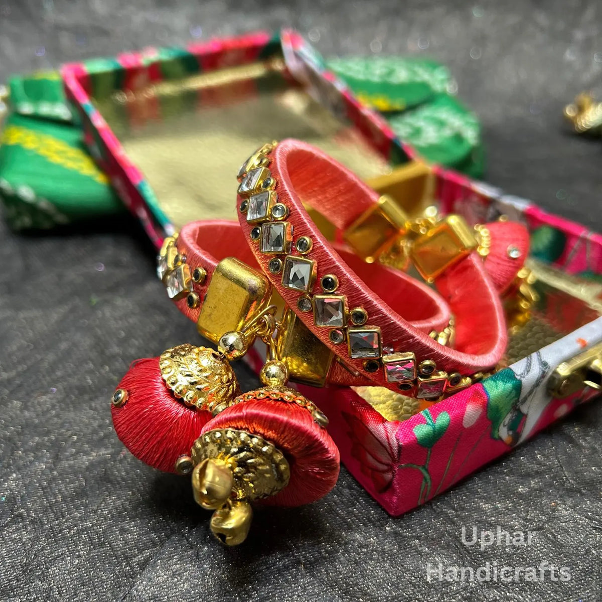 Peach Handcrafted silk thread bangles with Kundan work
Decorative stones arranged across the bangle surface
Gold-tone accents complement the silk thread wrapping
Jhumka latkan adds a hanging ornamental detail
Push-open clasp for wearing and removal
Traditional Indian accessories for special occasions
Uphar Handicrafts